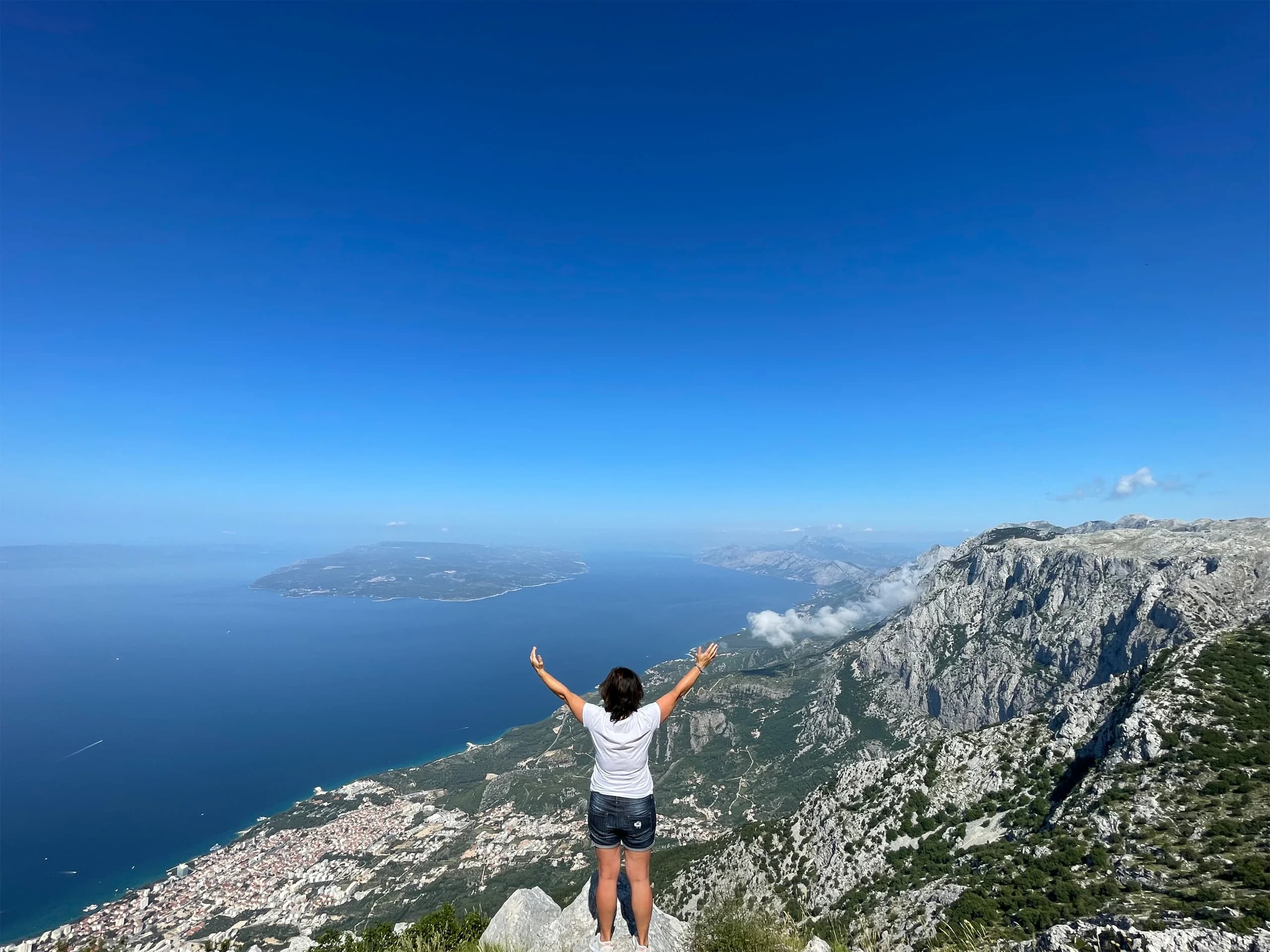 Žena s podignutim rukama uživa u pogledu s planine Biokovo s pogledom na Jadransko more