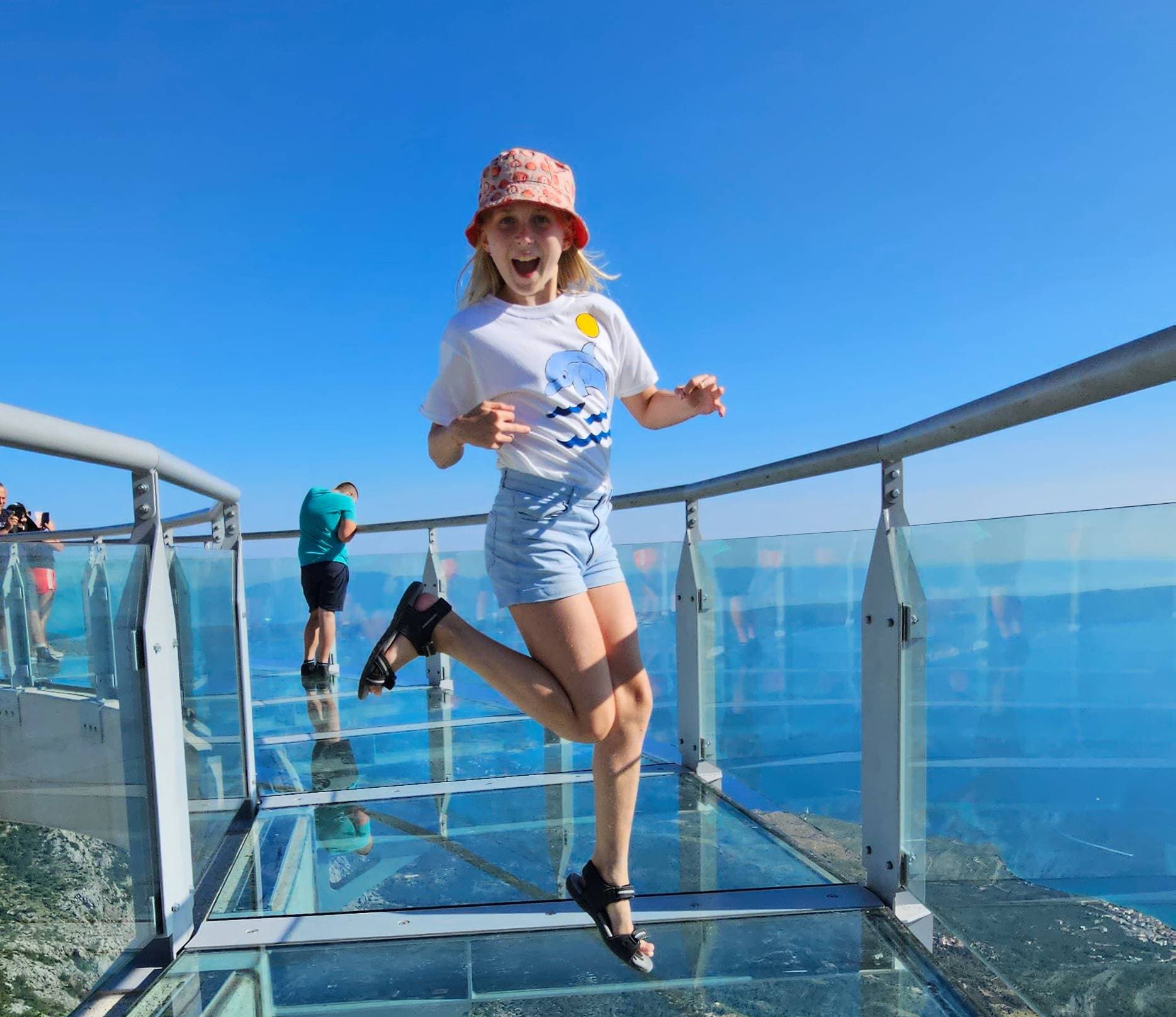 Dijete skače od radosti na staklenom mostu Skywalk na Biokovu s pogledom na nebo i more