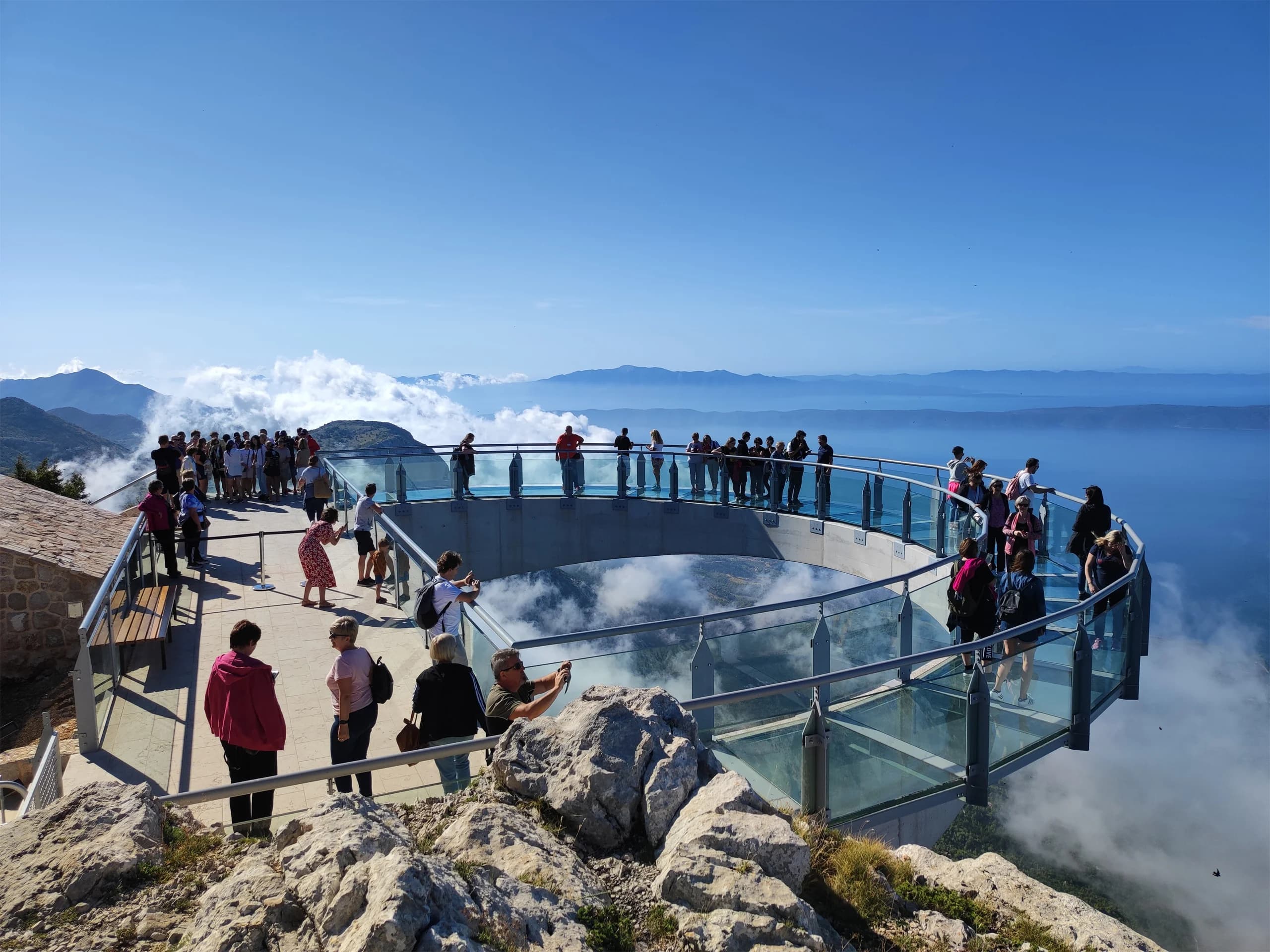 Posjetitelji na staklenoj vidikovci Skywalk iznad planine Biokovo s oblacima ispod